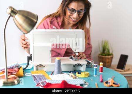 Happy latino sarta donna cucire con macchina maschera medica artigianale per prevenire e fermare la diffusione del virus corona Foto Stock