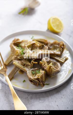 Carciofi italiani cotti sul piatto bianco con limone Foto Stock