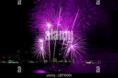 Meravigliosi fuochi d'artificio rosa viola che esplodono nel cielo notturno sulla città Foto Stock