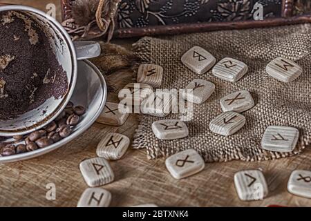 Concetto isoterico di divinazione e predizione. Rune, caffè in una tazza, rosario su un tavolo sullo sfondo di un vecchio petto Foto Stock