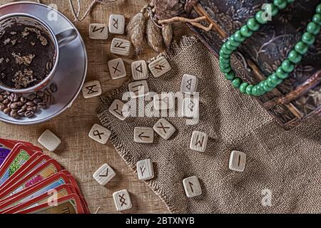 Concetto isoterico di divinazione e predizione. Carte Tarocchi, rune, caffè in una tazza, rosario su un tavolo sullo sfondo di un vecchio petto Foto Stock