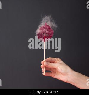 Lollipop rosa con capelli appiccicosi in una mano femminile su sfondo nero. Il concetto di salone di bellezza, epilazione, depilazione. Depilazione di cera, sugosa Foto Stock