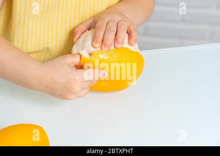 4 anni ragazza in una blusa gialla si siede ad un tavolo in cucina e spilla un pompelmo Foto Stock
