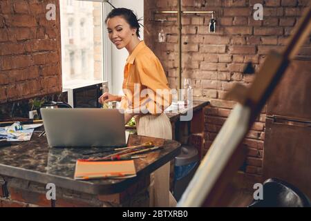 Bella signora che chiacchiera con un amico attraverso la videochiamata in cucina Foto Stock