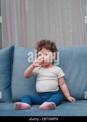 Il bambino di due anni si siede sul divano in una sala a casa Foto Stock