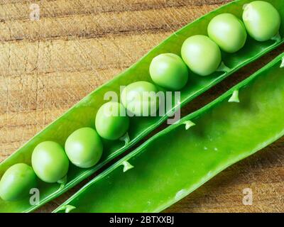 Piselli da giardino freschi in un cestino aperto su un tagliere di legno Foto Stock