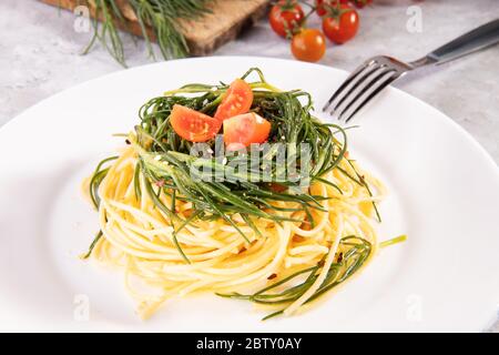 Spaghetti con agreetti, una verdura di primavera italiana, e ingredienti e forchetta su un piatto bianco su fondo grigio Foto Stock