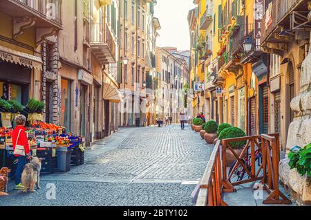 Brescia, Italia, 11 settembre 2019: Tipica stradina italiana con antichi edifici tradizionali, strada acciottolata, negozio di frutta e verdura e persone a piedi, centro storico, Lombardia Foto Stock