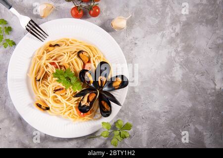 Tipici spaghetti di pasta italiana con cozze e pomodori su un piatto bianco con ingredienti su fondo grigio Foto Stock