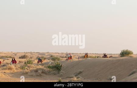 Un cammelliere (autista del cammello) che porta il cammello decorato mentre parla sui loro cellulari sulle dune di sabbia di sam del deserto di Thar con i turisti durante il tramonto Foto Stock