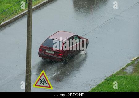 San Pietroburgo, Russia - 9 giugno 2019: Una macchina sta guidando su una strada bagnata sotto la pioggia e un cartello stradale 'attenzione ai bambini' vista dall'alto Foto Stock