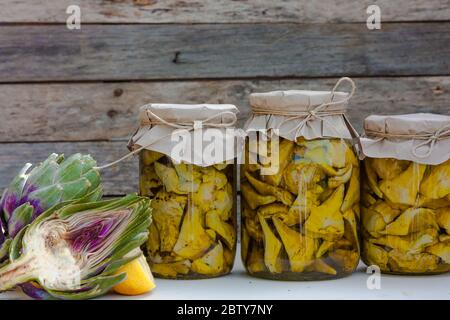 Carciofi conservati in olio d'oliva in vasetti di vetro su sfondo ligneo. Verdure di autunno che inscatolano. Cibo sano fatto in casa Foto Stock