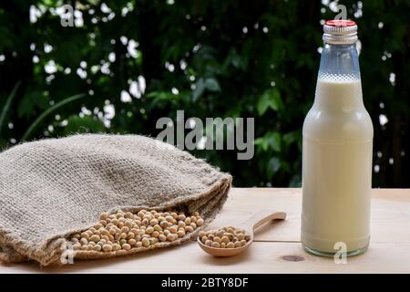 Latte di soia in bottiglie e soia su un cucchiaio versato fuori dal sacco di canapa sul pavimento di legno Foto Stock