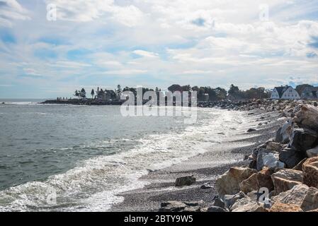 Cove e spiaggia di ghiaia lungo la costa del New Hampshire in una giornata soleggiata autunno. Una strada costiera fiancheggiata da edifici residenziali è visibile sullo sfondo. Foto Stock