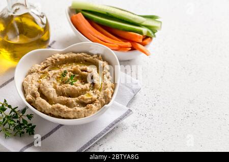 salsa di hummus in un recipiente, semi di sesamo, olio d'oliva, cetrioli e carote su sfondo chiaro Foto Stock