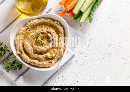 salsa di hummus in un recipiente, semi di sesamo, olio d'oliva, cetrioli e carote su sfondo chiaro Foto Stock