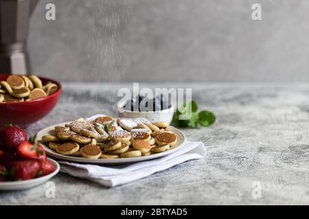 Minuscoli pancake per colazione. Frittelle di cereali con mirtilli, banane, fragole su sfondo grigio. Cibo alla moda. Spazio di copia per testo o disegno Foto Stock