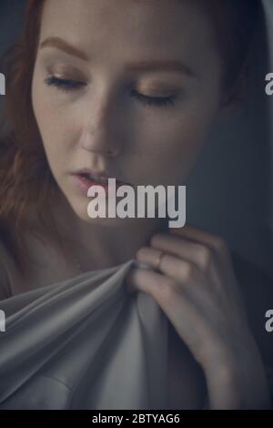 La ragazza dai capelli rossi guarda verso il basso e preme il tessuto sul petto. Incorniciate la tenda. Mettere a fuoco il viso. Foto Stock