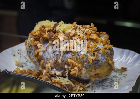 Patate intere al forno con formaggio e cipolla fritta, patatine fritte in coni di carta, macchina sullo sfondo, festival di Street food, fast food. FR Foto Stock