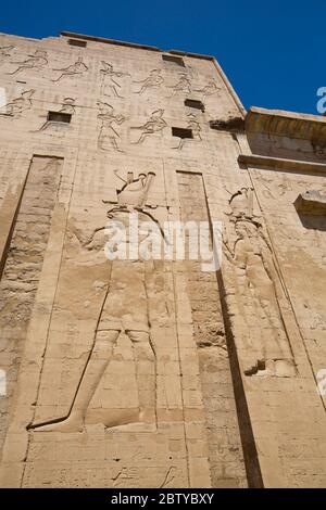 Bas Sollievo di Dio Horus a sinistra, primo Pylon, Tempio di Horus, Edfu, Egitto, Africa del Nord, Africa Foto Stock