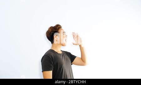 Giovane uomo asiatico felice annunciare informazioni con le mani alla bocca isolato su sfondo bianco studio, banner e con spazio di copia Foto Stock