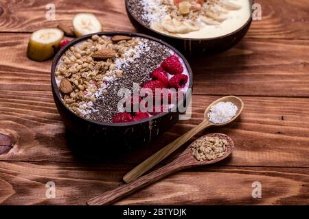 Lamponi e semi di chia in ciotole di frullato con frutti di bosco congelati e muesli.nutrizione sana in cocco naturale.sano cibo vegano concetto. Foto Stock