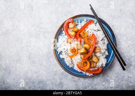 Ciotola di tofu vegana con riso, pepe, carote e cumino in una ciotola di ceramica, fondo grigio. Foto Stock