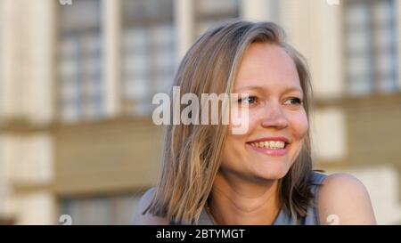 Bella bionda sorridente accogliente seduta all'aperto. Foto Stock