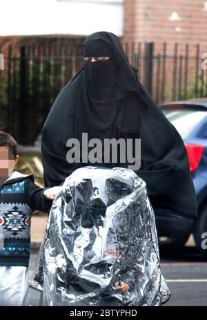 Una donna cammina su una strada britannica indossando una copertura Burka faccia, Birmingham, Inghilterra. Foto Stock