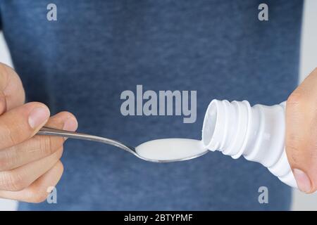Chiudere la mano versando il farmaco dal flacone al cucchiaio. Assistenza sanitaria e concetto medico. Foto Stock