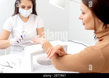 Manicure sta applicando antisettico sulle mani del cliente in manicure salone. Foto Stock