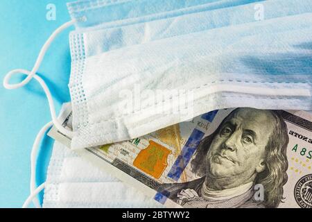 Maschera facciale e banconota da 100 dollari su sfondo blu. Concetto di deficit, speculazione e carenza di maschere mediche in vendita. Messa a fuoco selettiva, clos Foto Stock