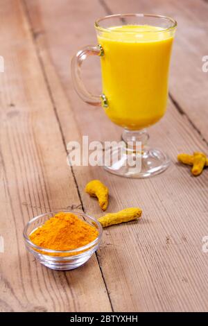 Latte dorato in una tazza grigia di vetro su sfondo di legno Foto Stock