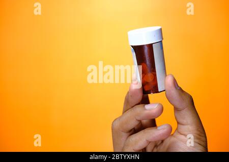mano del giovane uomo che tiene un contenitore della pillola contro sfondo arancione Foto Stock