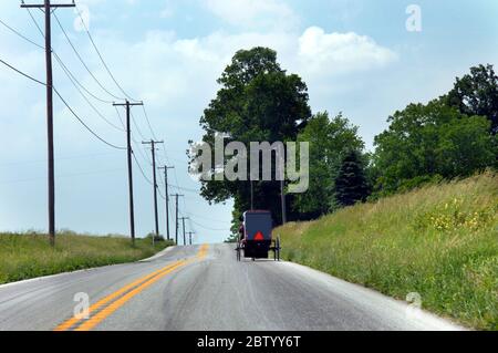 Amish buggy percorre un'autostrada di campagna. Il buggy sta sommando una collina. Foto Stock