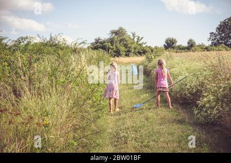 due bambini piccoli con reti in mano che catturano farfalle in verde campagna Foto Stock