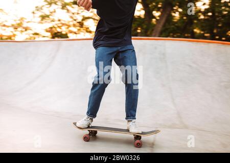 Primo piano skater boy in T-shirt e jeans che si esercitano in moderno skate Park Foto Stock