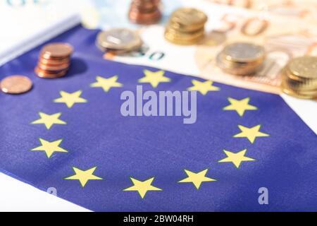 Stimolo finanziario dell'Unione europea sul concetto pandemico del Coronavirus Covid-19. Bandiera dell'Unione europea con banconote e monete in euro Foto Stock