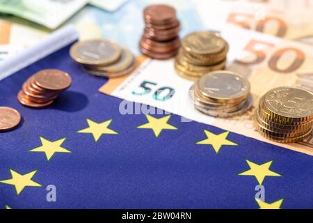 Stimolo finanziario dell'Unione europea sul concetto pandemico del Coronavirus Covid-19. Bandiera dell'Unione europea con banconote e monete in euro Foto Stock