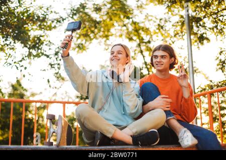 Giovane skater ragazzo e ragazza con le cuffie che girano felicemente sulla fotocamera mentre registra nuovi video insieme allo skatepark Foto Stock