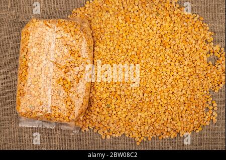 Piselli spezzati gialli in un sacchetto di plastica e cereali sfusi su uno sfondo di tela con una consistenza ruvida. Cereali tradizionali per la preparazione di zuppe e porridg Foto Stock