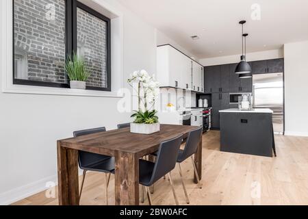 Una sala da pranzo e una cucina con mobili da cucina bianchi e grigio scuro. Un fiore è sul tavolo come un centropiece con quattro sedie al tavolo di legno. Foto Stock