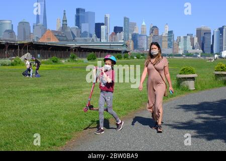 Una donna con una ragazza giovane che indossa una maschera a piedi nel Liberty state Park con lo skyline del quartiere finanziario di New York City sullo sfondo.Jersey City.New Jersey.USA Foto Stock