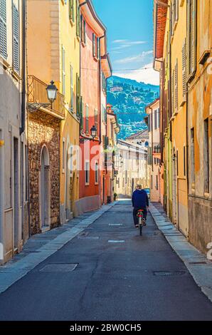 Brescia, Italia, 11 settembre 2019: Tipica strada italiana con antichi edifici colorati con mura multicolore e uomo in bicicletta su strada, verde collina, centro storico, vista verticale, Lombardia Foto Stock