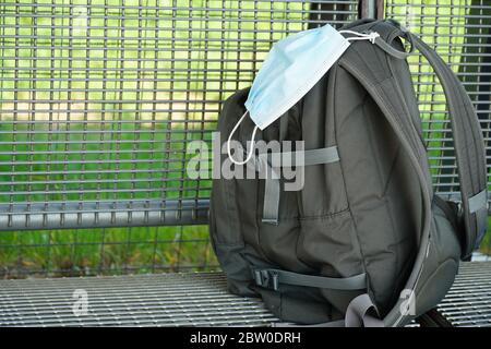 Uno zaino con una maschera facciale N95 attaccata su una banca metallica di una stazione ferroviaria durante il Lockdown a causa del coronavirus, covid-19 con il suo blocco Foto Stock