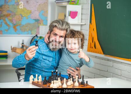 Ragazzo concentrato - padre e figlio seduti al tavolo e giocando a scacchi. Il figlio gioca a scacchi con padre e sorride a casa Foto Stock