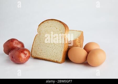 Studio girato su bianco di alimenti di base pane, uova e patate. Foto Stock