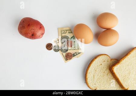 Uno studio girato su bianco guardando giù su alimenti di base uova, pane e patate con valuta che rappresenta l'economia Foto Stock