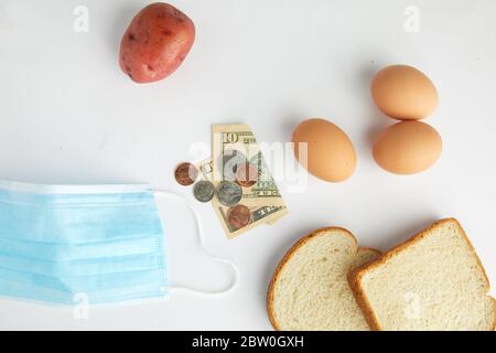 Top down studio girato su alimentari punti di cottura uova, pane e patate una maschera chirurgica viso e valuta che illustra l'economia e coronavirus. Foto Stock