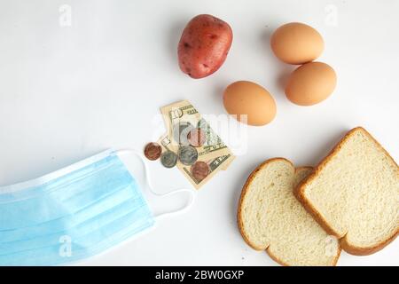 Top down studio girato su alimentari punti di cottura uova, pane e patate una maschera chirurgica viso e valuta che illustra l'economia e coronavirus. Foto Stock